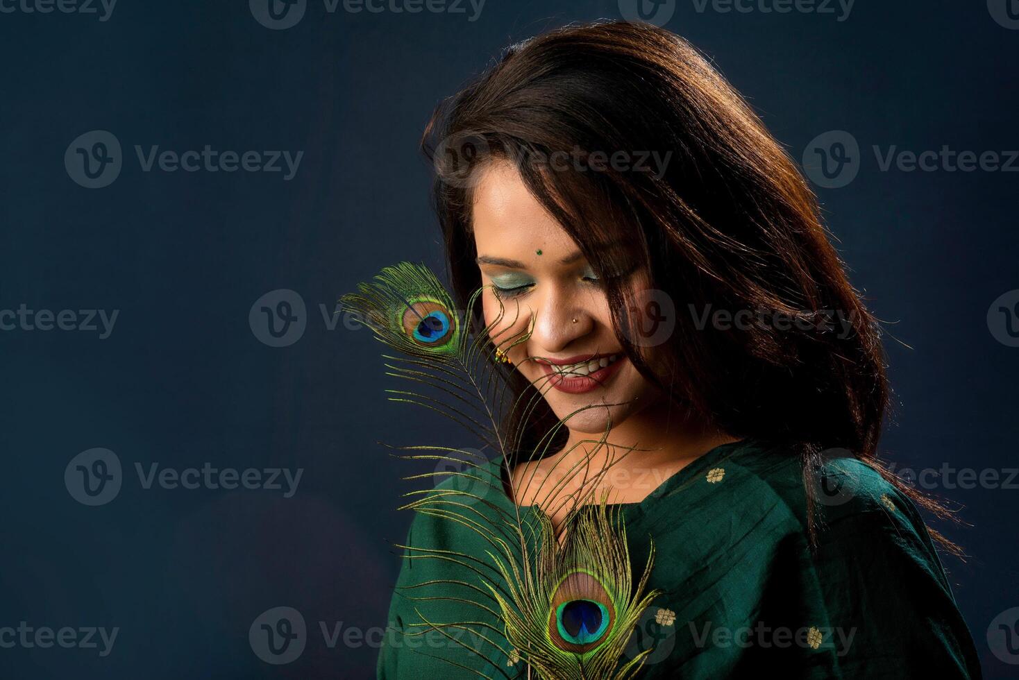 Beautiful Young Girl posing with peacock feathers on grey background. photo