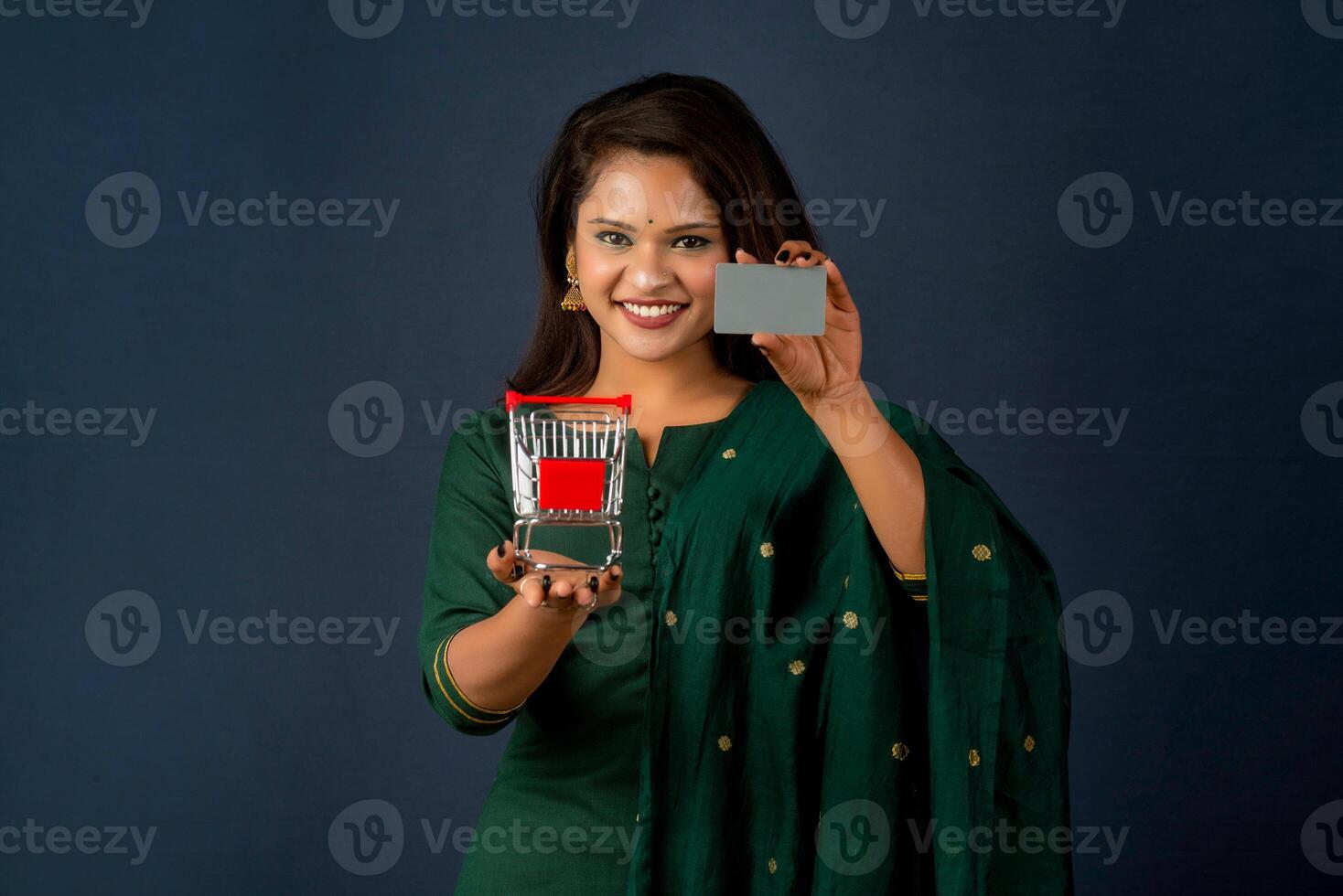 Beautiful young girl or woman holding and posing with a miniature trolley shopping cart with credit or debit cards on a gray background photo