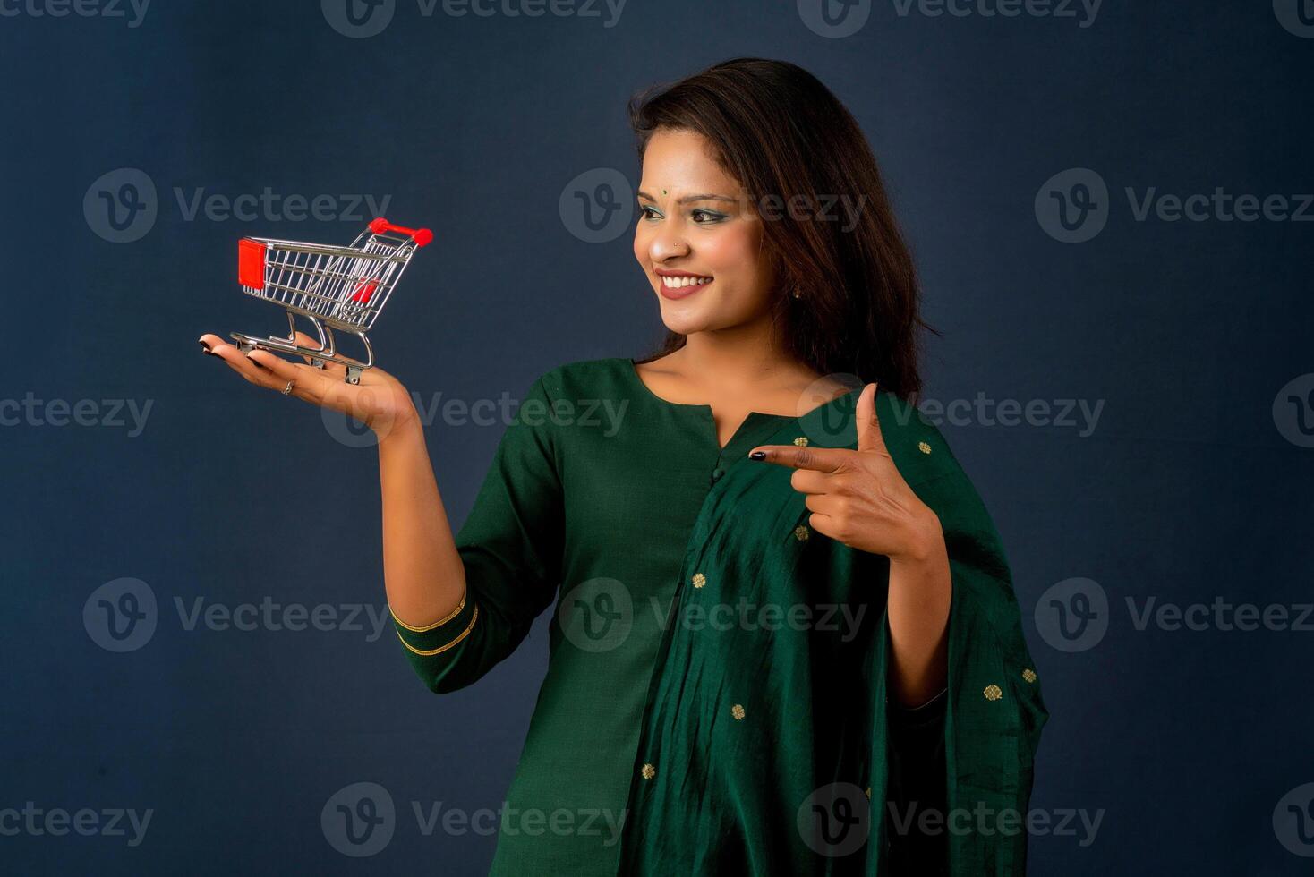 Happy young Smiling girl with a miniature trolley shopping cart on the gray background. Beautiful girl in shopping concept. photo
