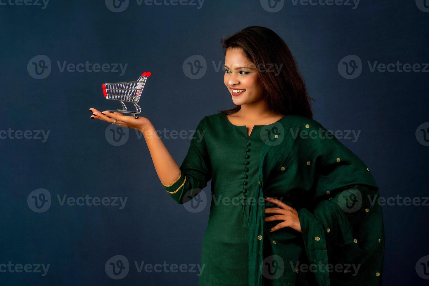 Happy young Smiling girl with a miniature trolley shopping cart on the gray background. Beautiful girl in shopping concept. photo