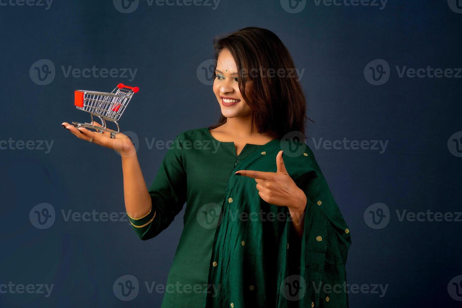 Happy young Smiling girl with a miniature trolley shopping cart on the gray background. Beautiful girl in shopping concept. photo