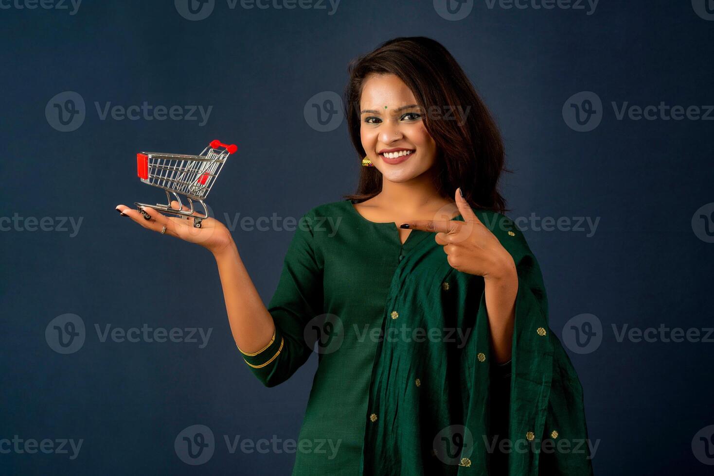 Happy young Smiling girl with a miniature trolley shopping cart on the gray background. Beautiful girl in shopping concept. photo