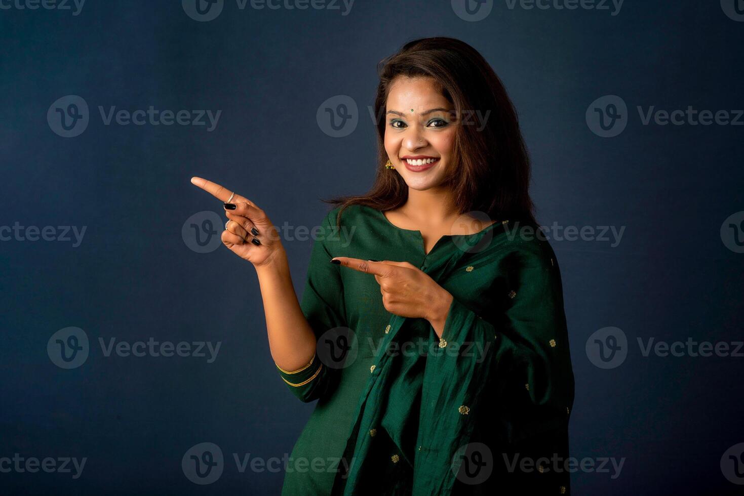 Portrait of a successful cheerful young girl presenting something with a fingers with a happy smiling face. photo