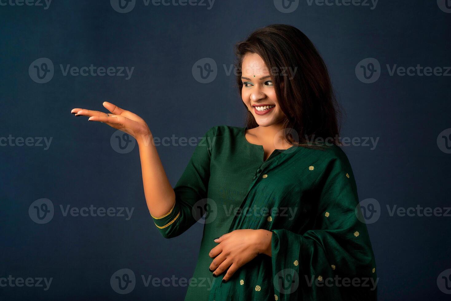 Portrait of a successful cheerful young girl holding and presenting something on hand with a happy smiling face. photo