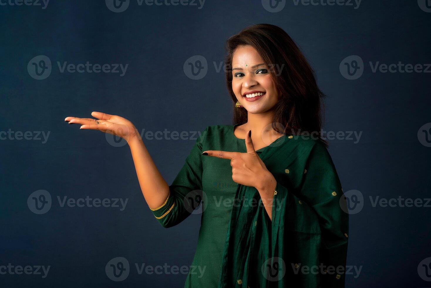Portrait of a successful cheerful young girl holding and presenting something on hand with a happy smiling face. photo
