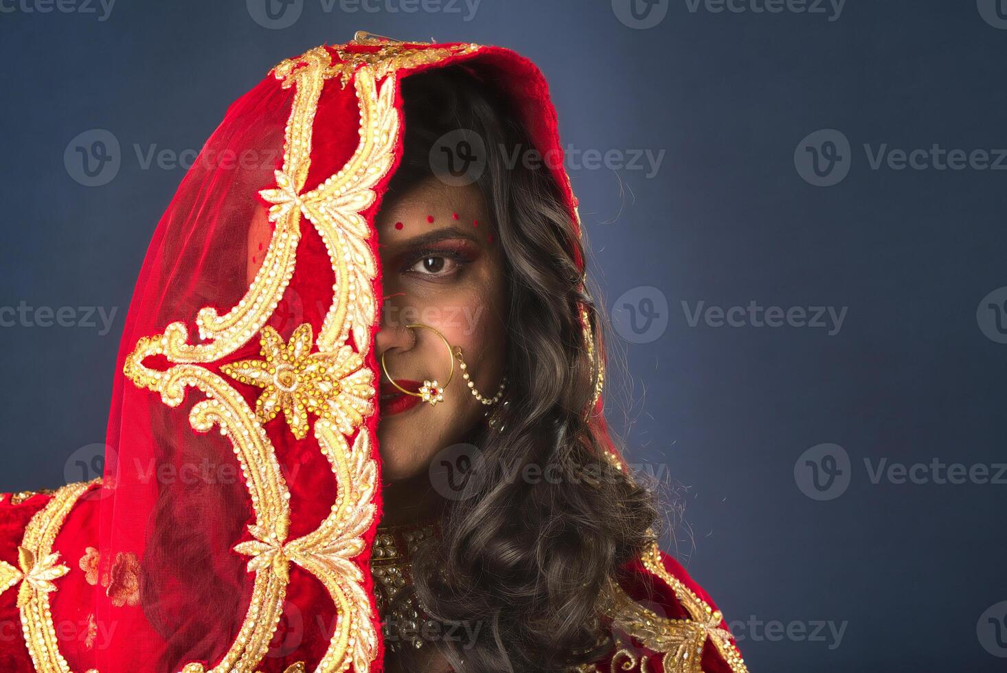 Young crossdresser man wearing Indian wedding clothes of a bride with bridal makeup and posing on grey background, looking fashion and glamorous. photo