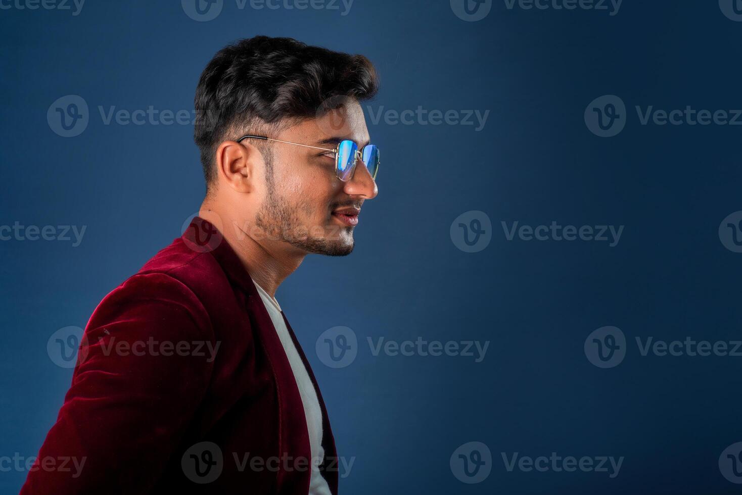 Portrait of Happy Indian young man wearing a blazer with eyeglasses posing on a blue background photo