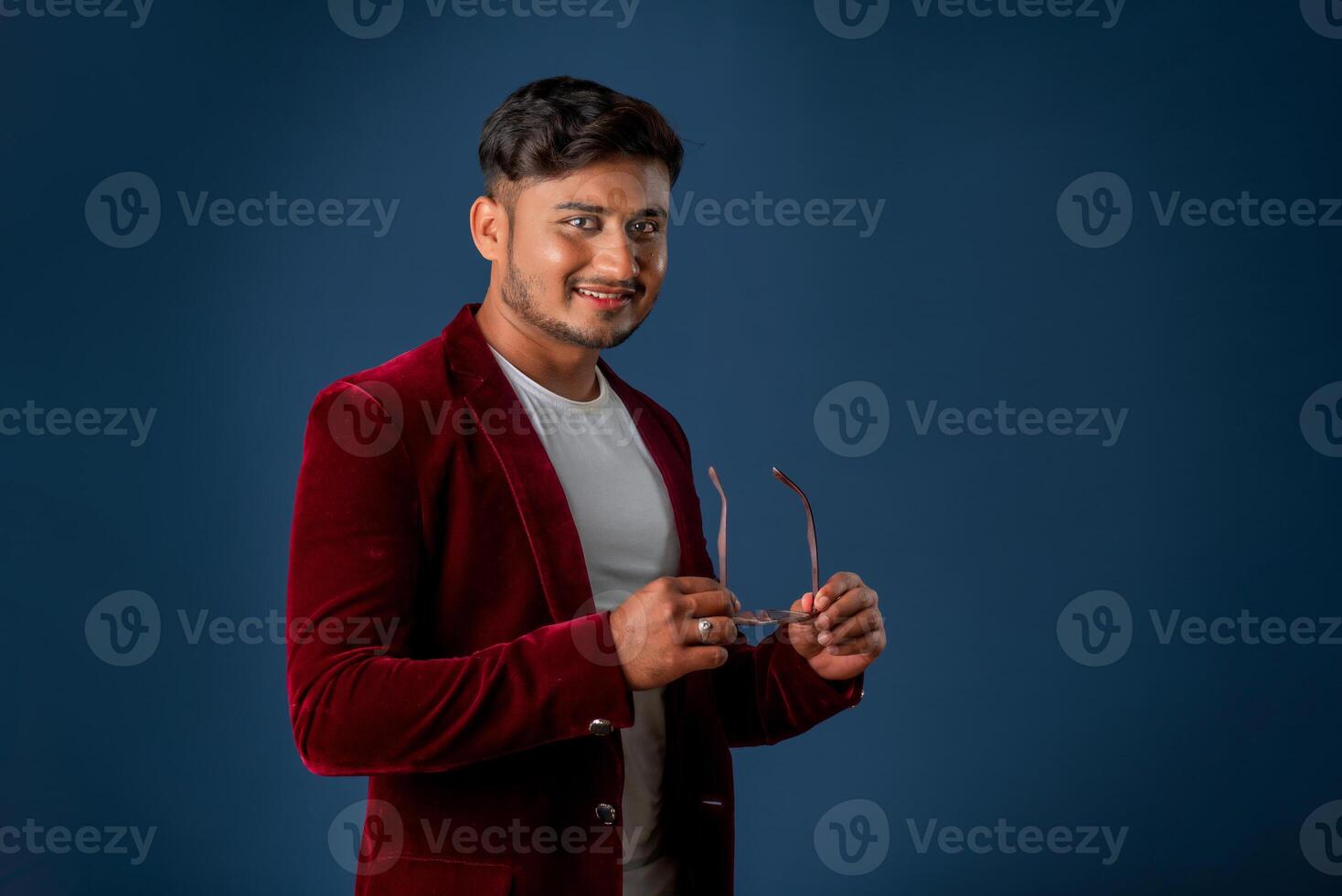 Portrait of Happy Indian young man wearing a blazer with eyeglasses posing on a blue background photo