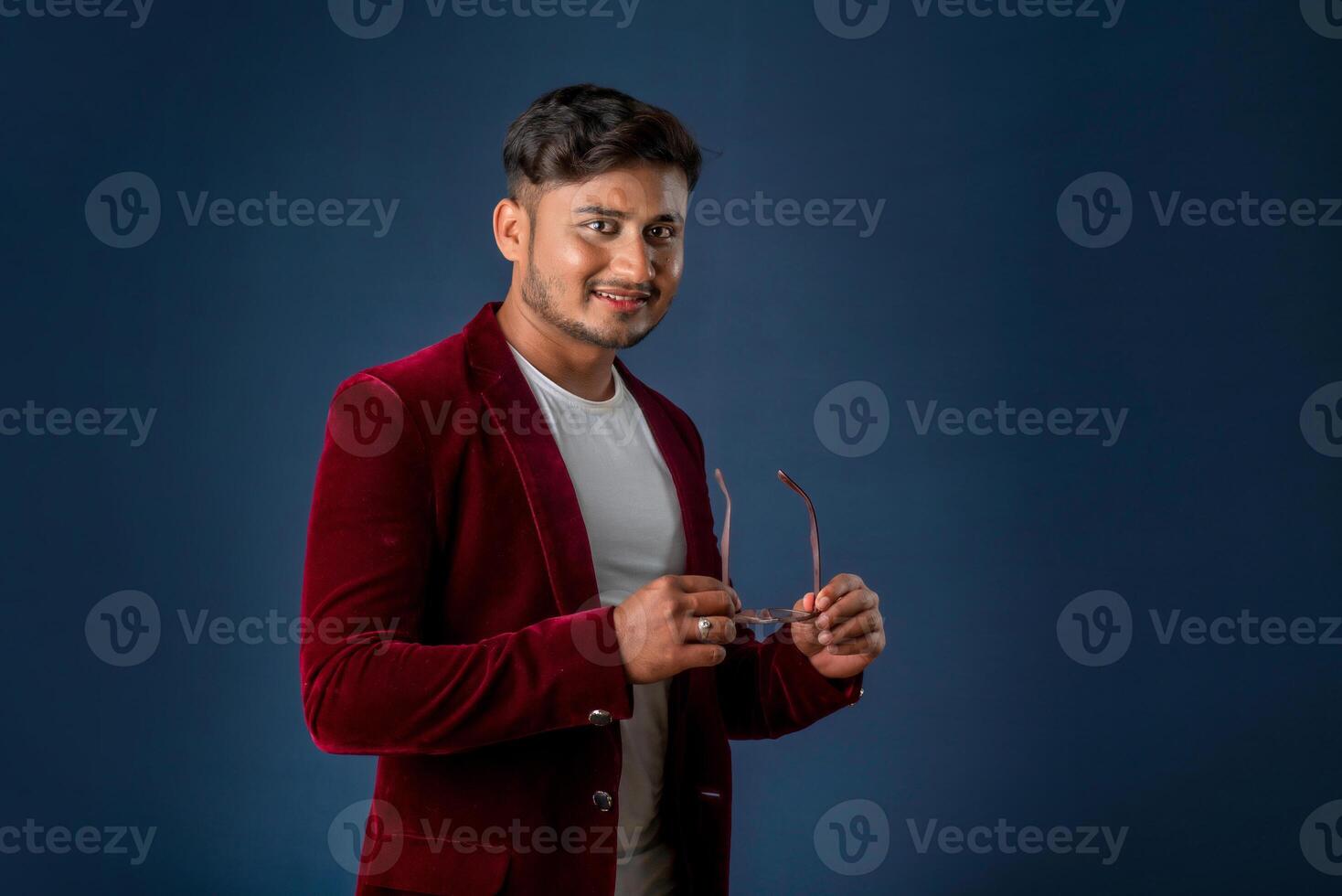 Portrait of Happy Indian young man wearing a blazer with eyeglasses posing on a blue background photo