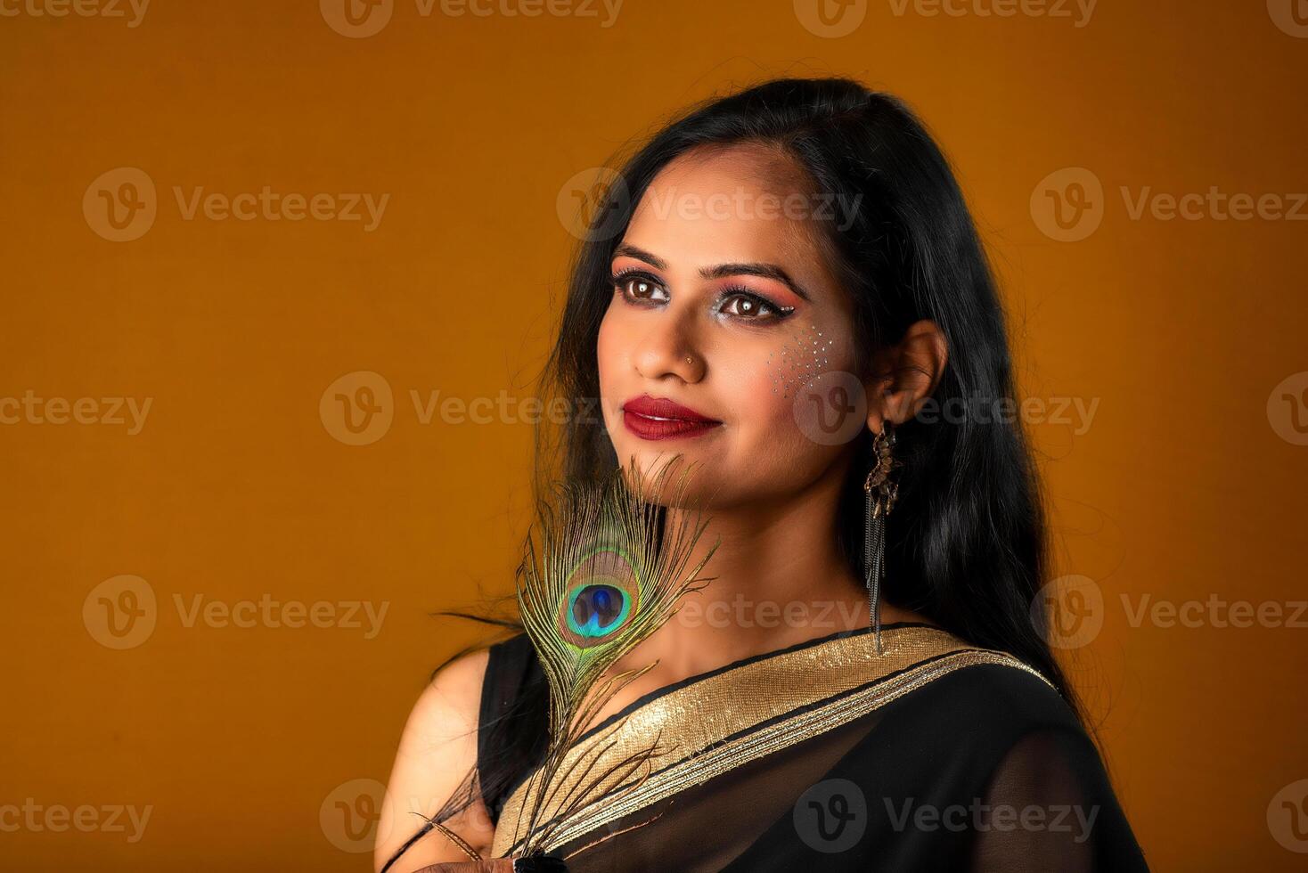 Beautiful Young Girl with bright makeup posing with peacock feathers on yellow background. photo