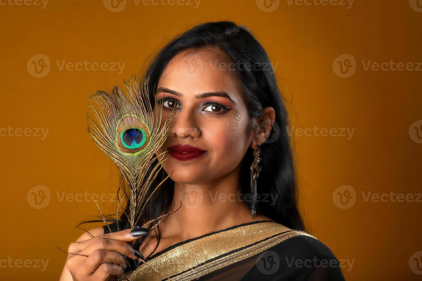 Beautiful Young Girl with bright makeup posing with peacock feathers on yellow background. photo