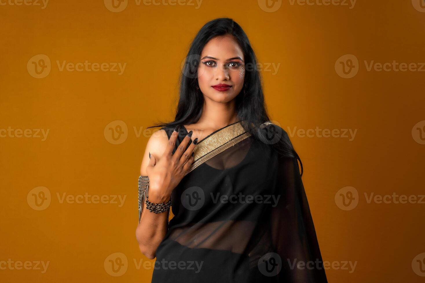 Portrait of a young beautiful girl wearing traditional black saree posing on a brown background. photo