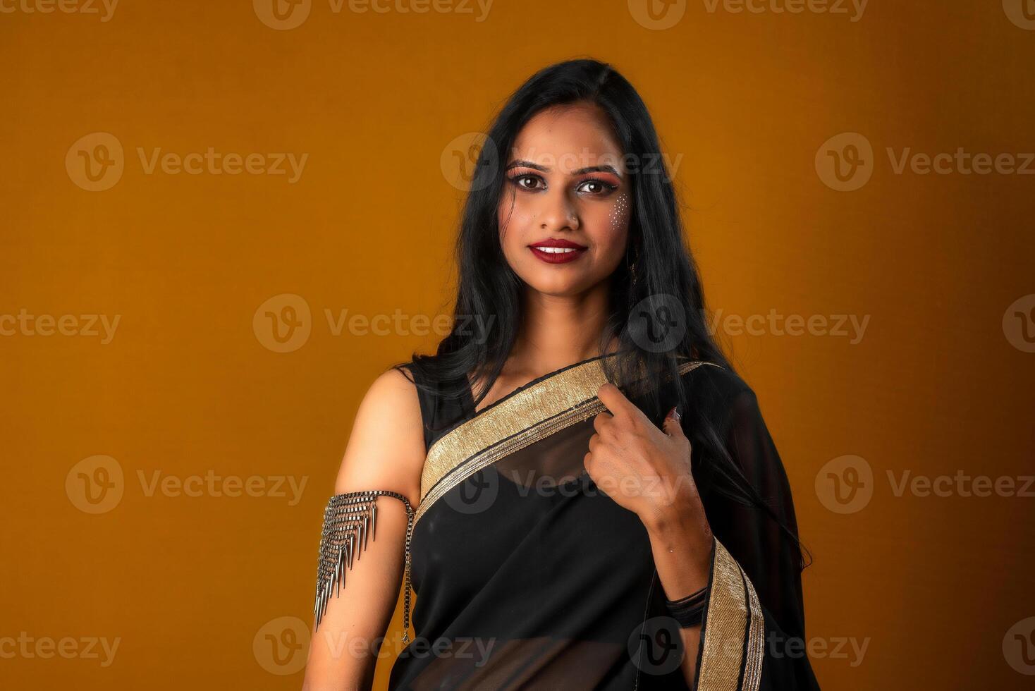 Portrait of a young beautiful girl wearing traditional black saree posing on a brown background. photo