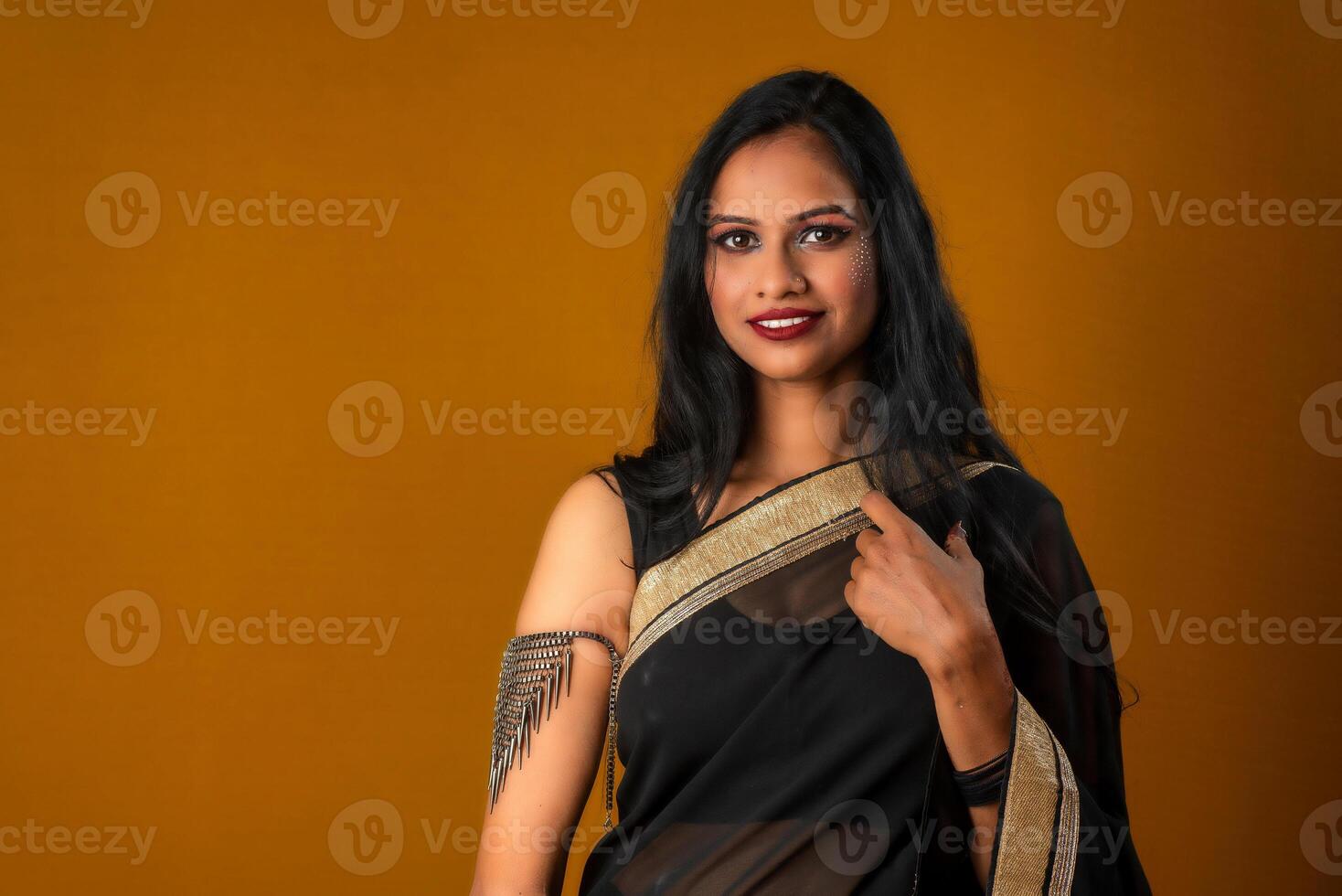 Portrait of a young beautiful girl wearing traditional black saree posing on a brown background. photo