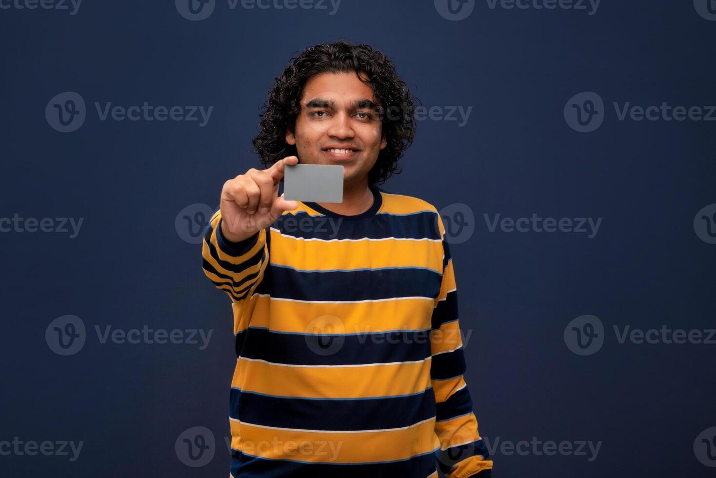 Young smiling handsome man posing with a credit or debit card on gray background. photo