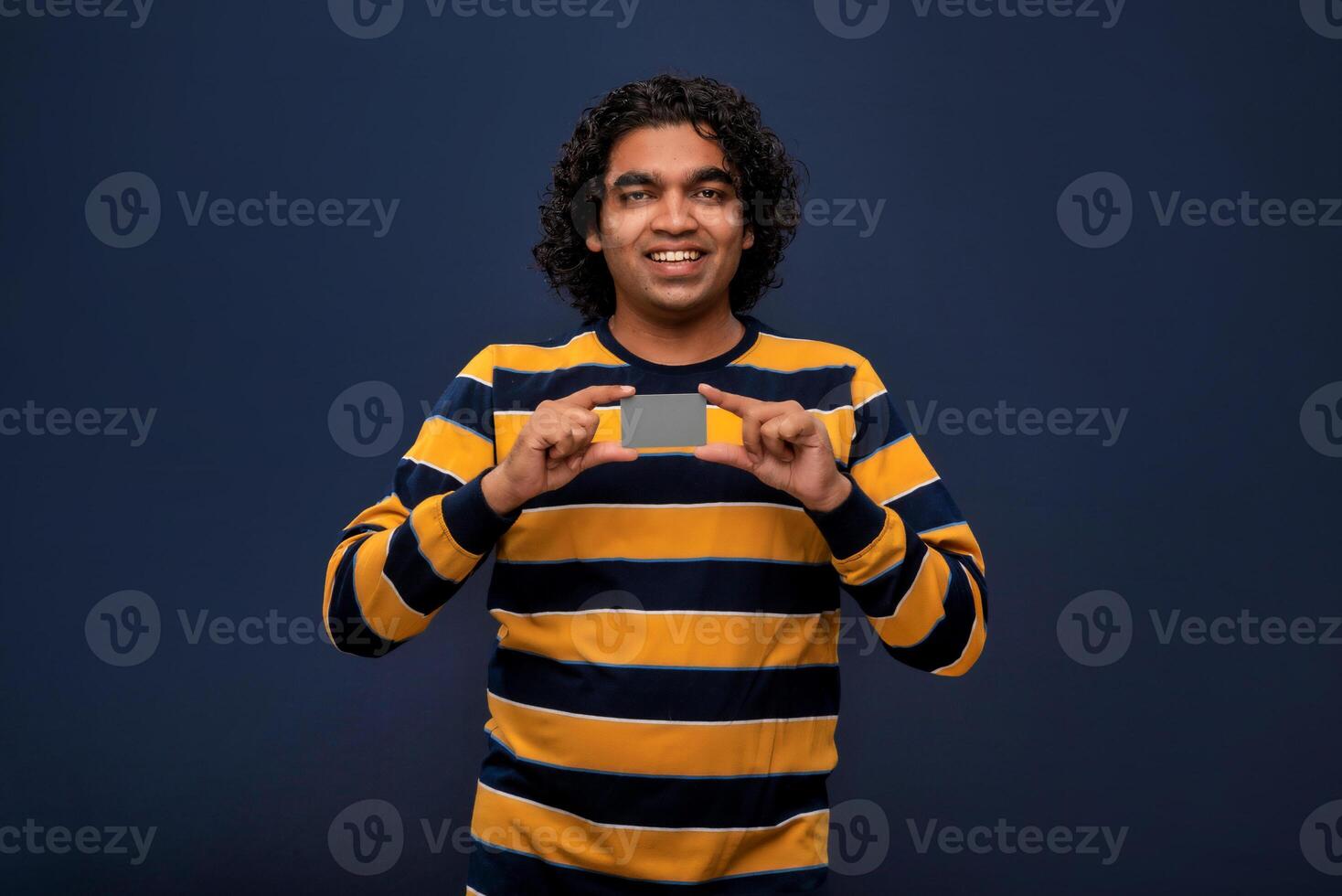 Young smiling handsome man posing with a credit or debit card on gray background. photo