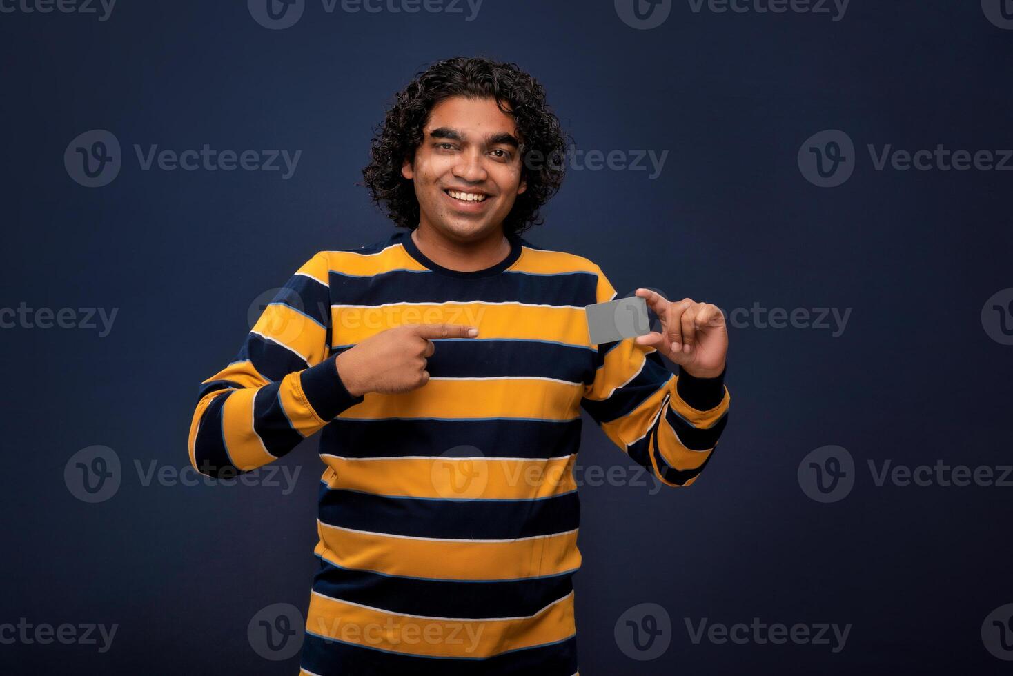 Young smiling handsome man posing with a credit or debit card on gray background. photo