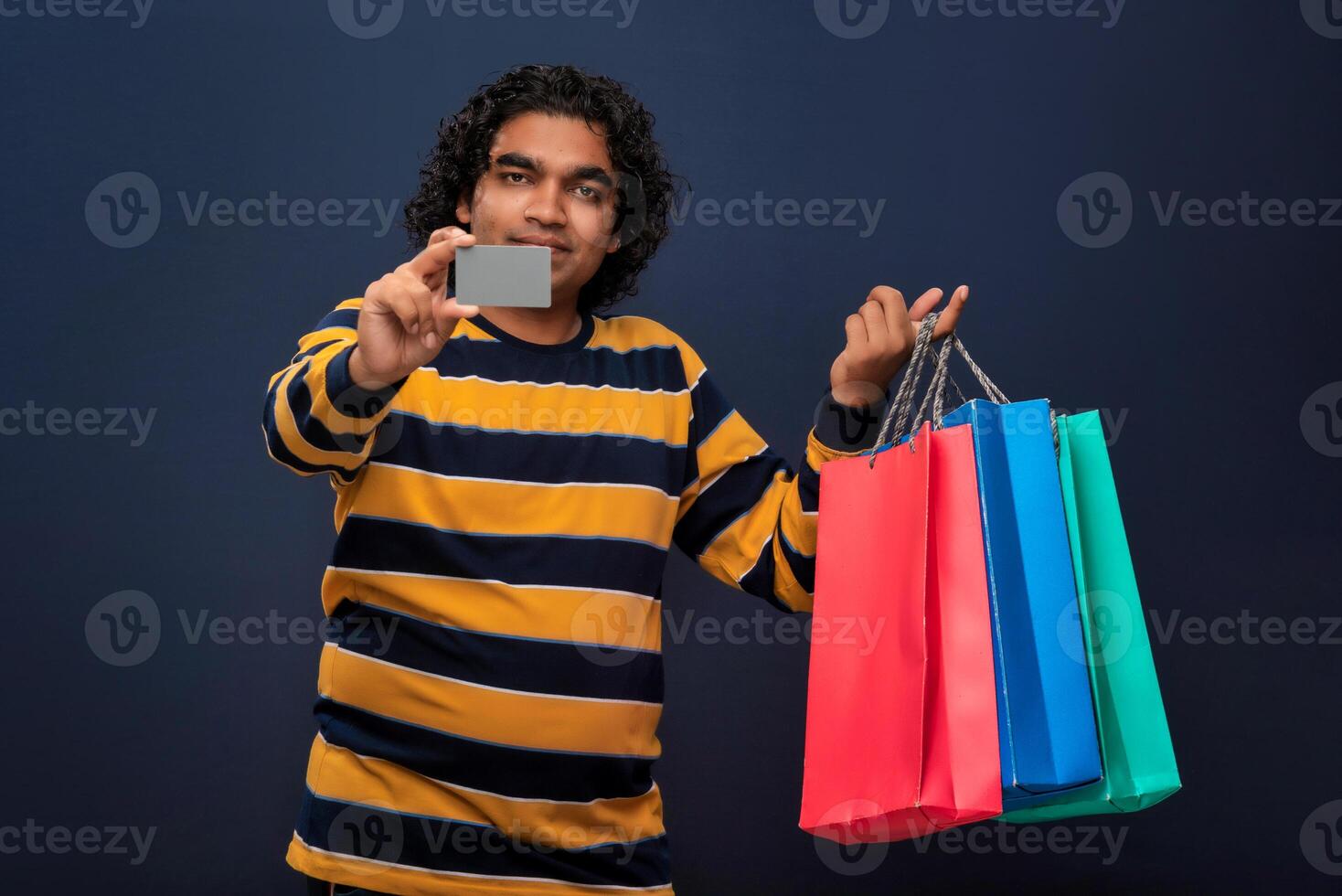 young man holding and posing with shopping bags with credit or debit card on a gray background photo