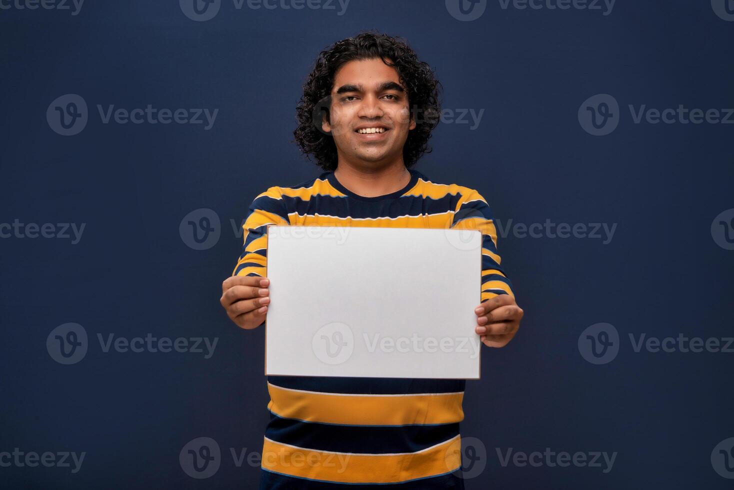 A happy young man holding and displaying a signboard or placard in his hands on a dark background. ready for your text or product. photo