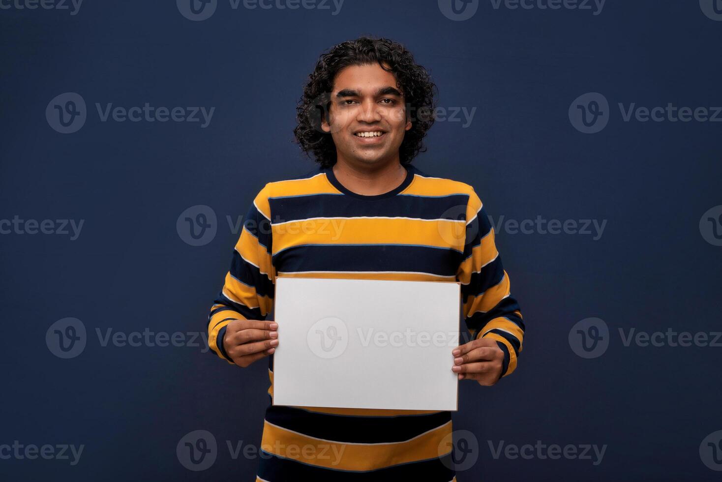 A happy young man holding and displaying a signboard or placard in his hands on a dark background. ready for your text or product. photo
