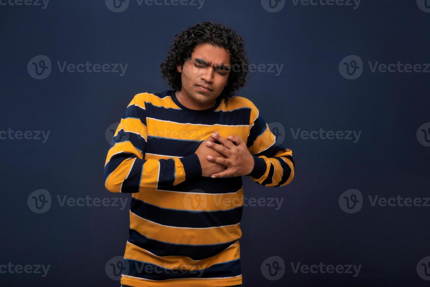 A man with curly hair and a striped shirt is holding his chest photo
