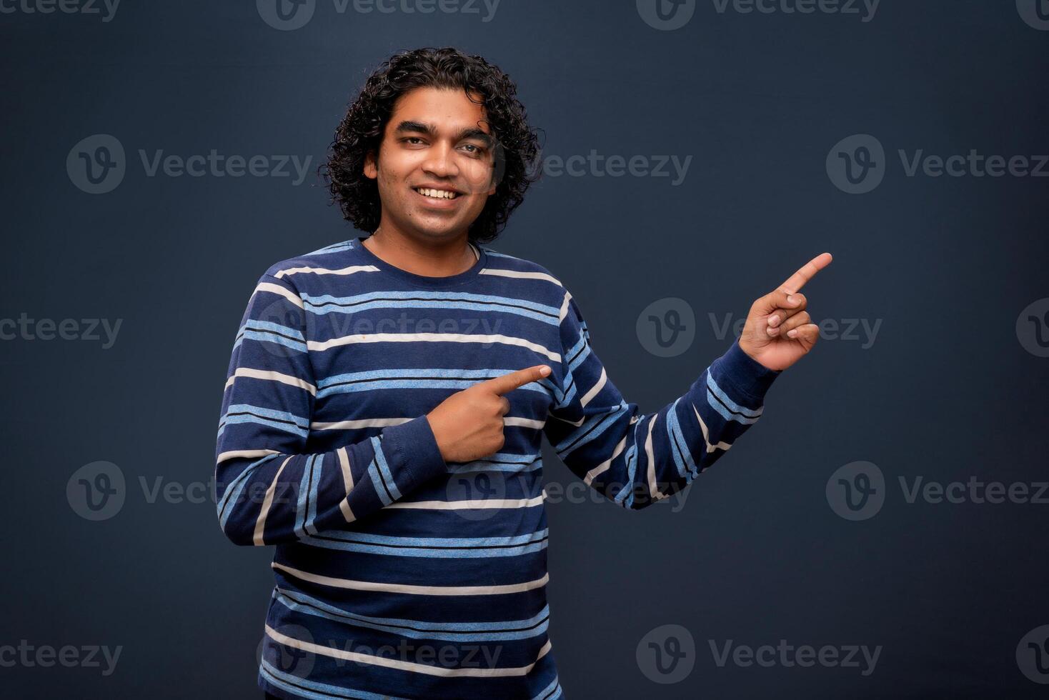 Portrait of a successful cheerful young man pointing and presenting something with hand or finger with a happy smiling face. photo