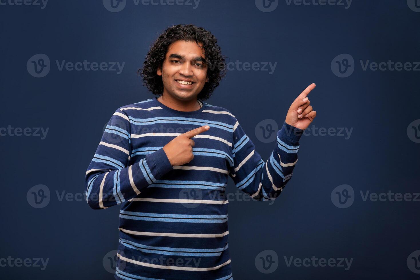 Portrait of a successful cheerful young man pointing and presenting something with hand or finger with a happy smiling face. photo