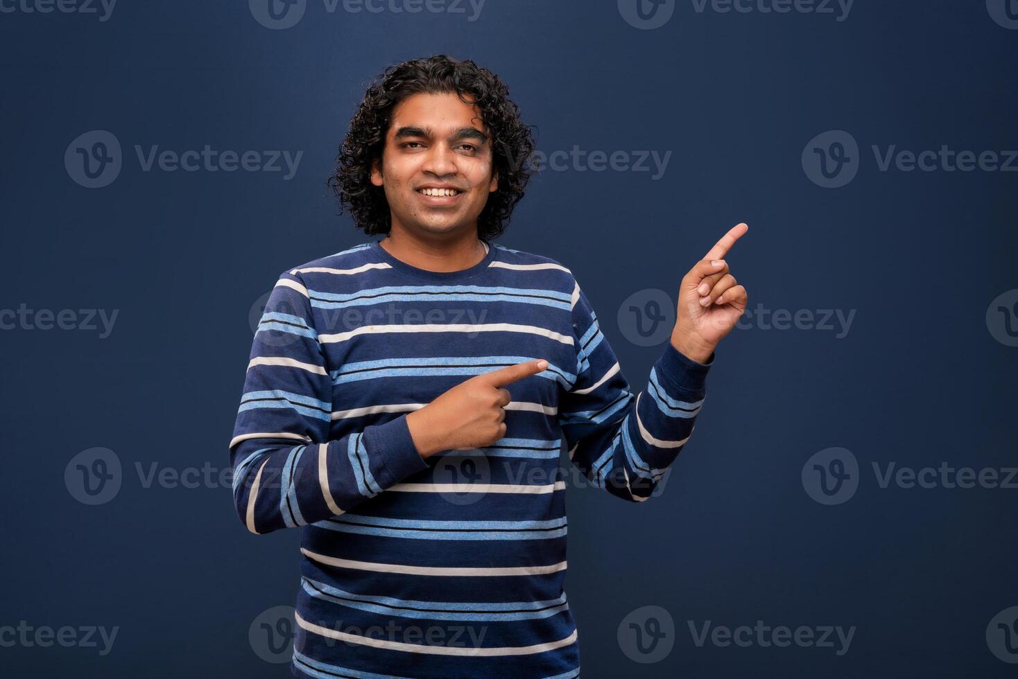 Portrait of a successful cheerful young man pointing and presenting something with hand or finger with a happy smiling face. photo