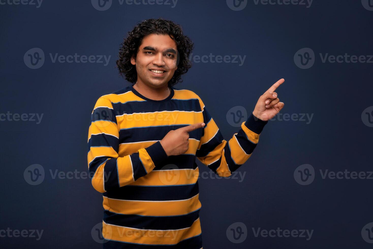 Portrait of a successful cheerful young man pointing and presenting something with hand or finger with a happy smiling face. photo