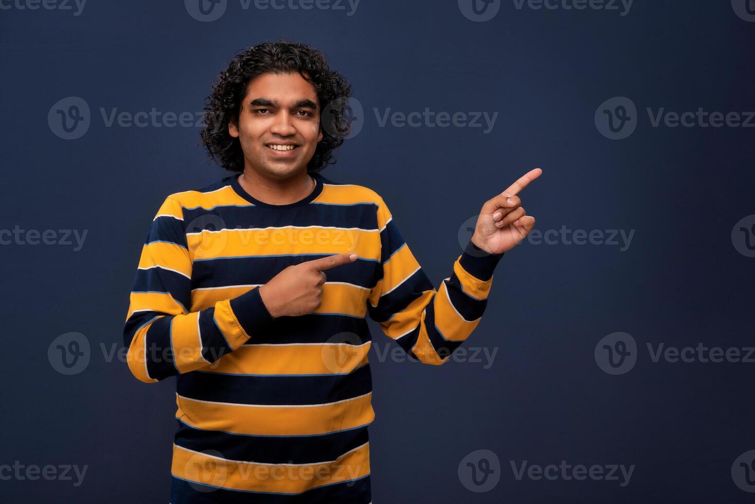 Portrait of a successful cheerful young man pointing and presenting something with hand or finger with a happy smiling face. photo