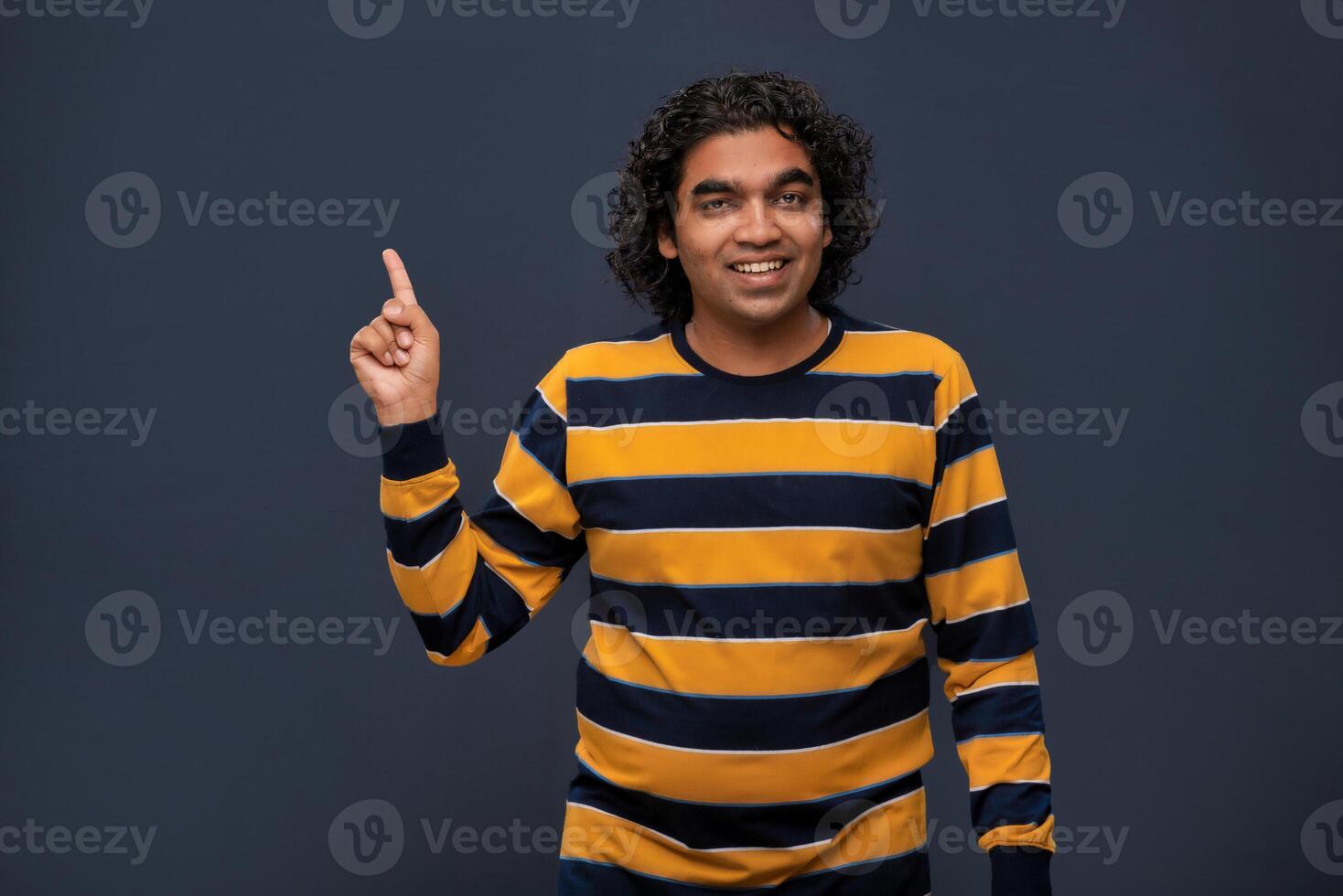 Portrait of a successful cheerful young man pointing and presenting something with hand or finger with a happy smiling face. photo