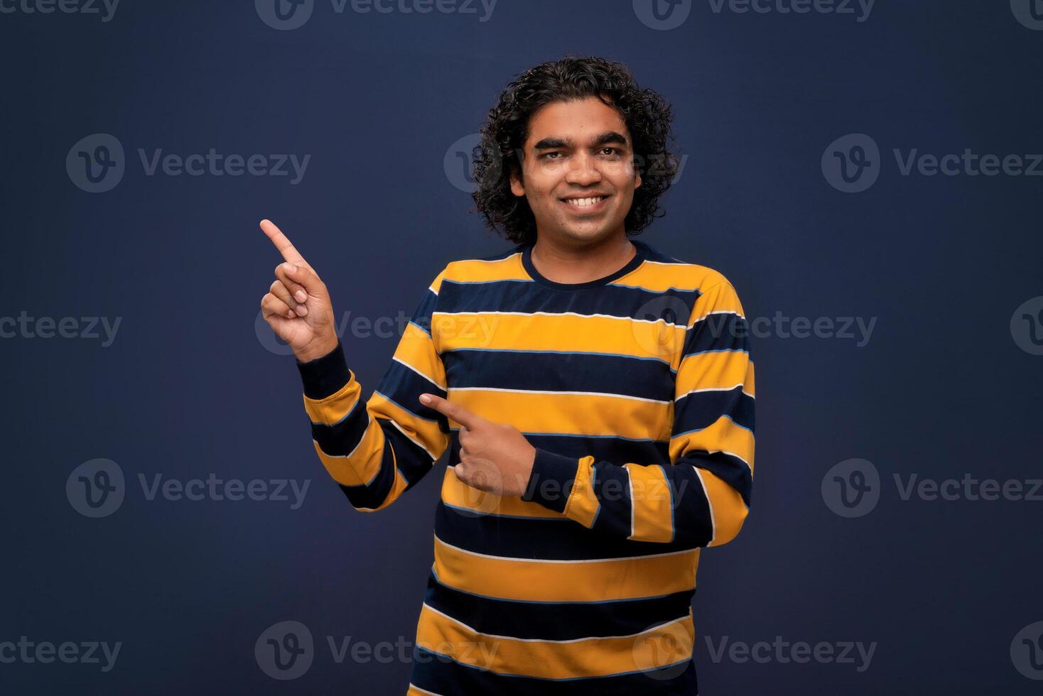 Portrait of a successful cheerful young man pointing and presenting something with hand or finger with a happy smiling face. photo
