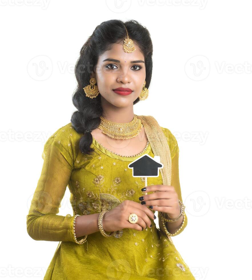 Happy Indian traditional young woman holding a little house cutout board in her hands on a white background. photo