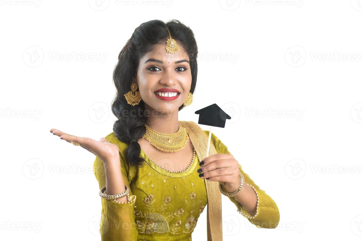 Happy Indian traditional young woman holding a little house cutout board in her hands on a white background. photo