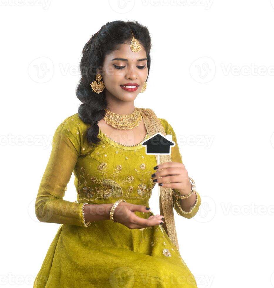 Happy Indian traditional young woman holding a little house cutout board in her hands on a white background. photo