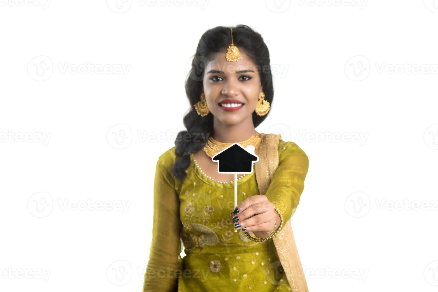 Happy Indian traditional young woman holding a little house cutout board in her hands on a white background. photo