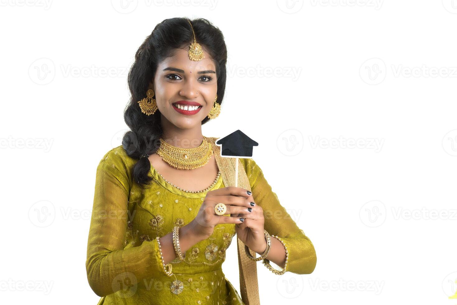 Happy Indian traditional young woman holding a little house cutout board in her hands on a white background. photo