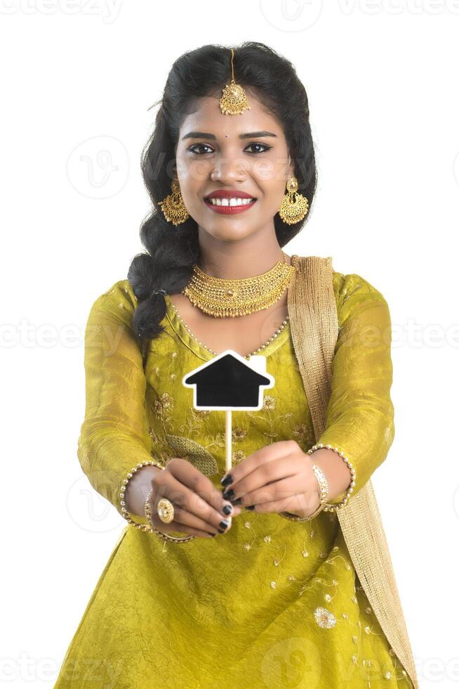 Happy Indian traditional young woman holding a little house cutout board in her hands on a white background. photo