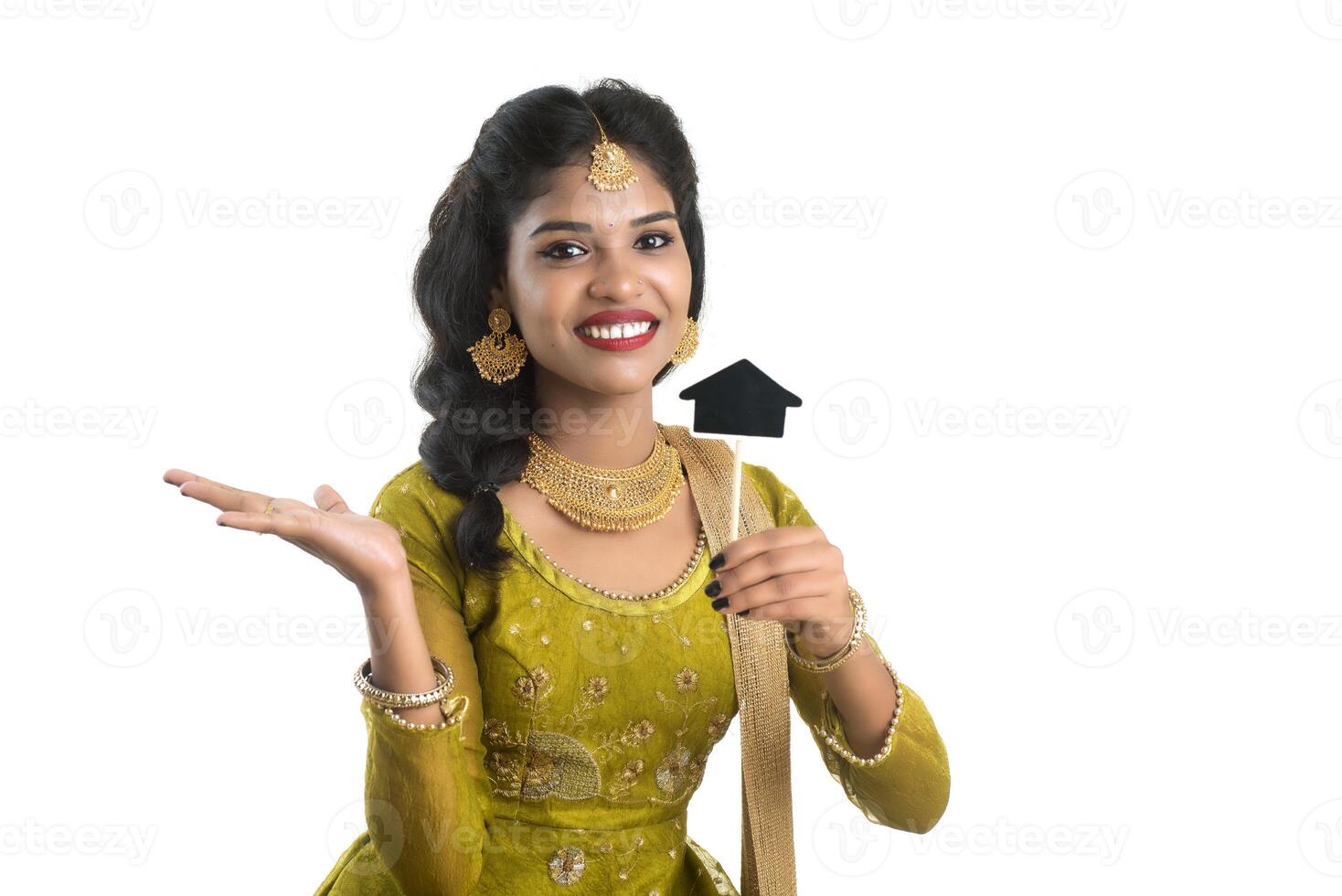 Happy Indian traditional young woman holding a little house cutout board in her hands on a white background. photo