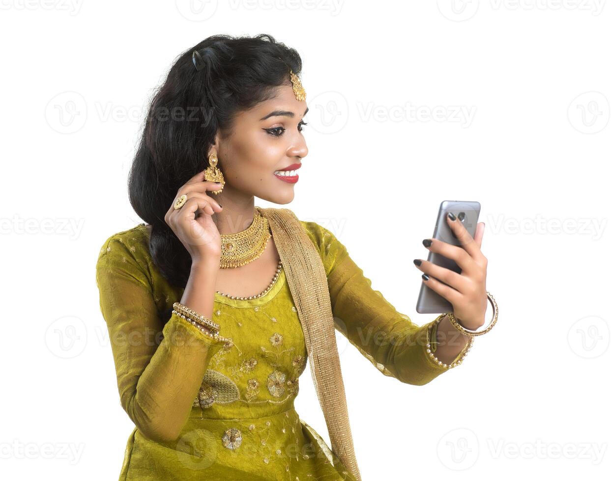 Young Indian traditional girl using a mobile phone or smartphone isolated on a white background photo
