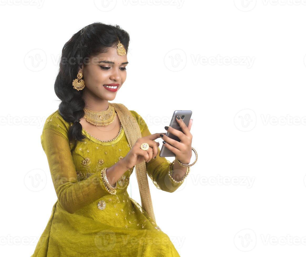 Young Indian traditional girl using a mobile phone or smartphone isolated on a white background photo