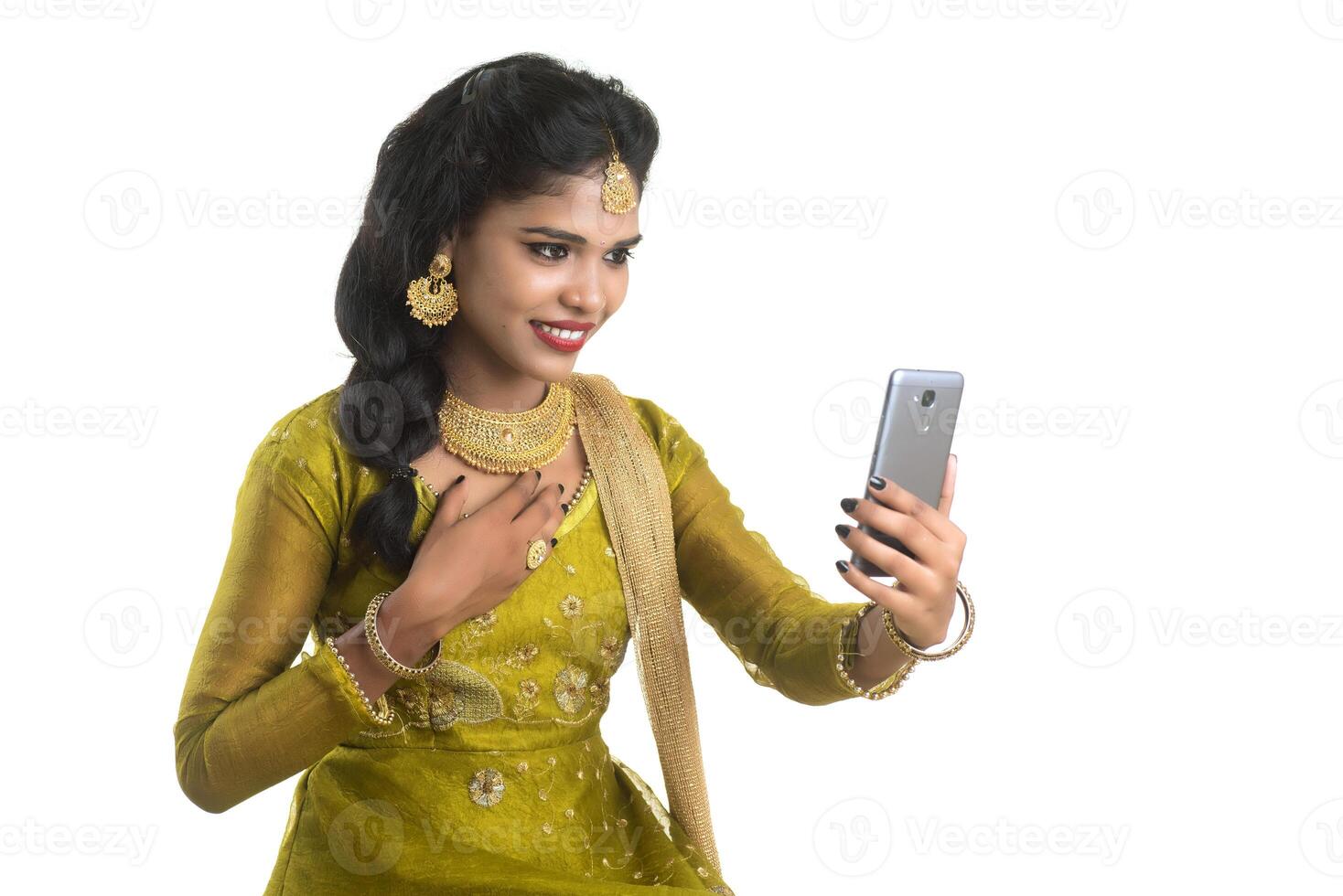 Young Indian traditional girl using a mobile phone or smartphone isolated on a white background photo