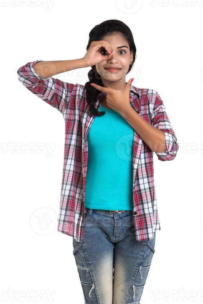 young woman looking at camera through fingers in ok gesture. Imitating binoculars over white background photo