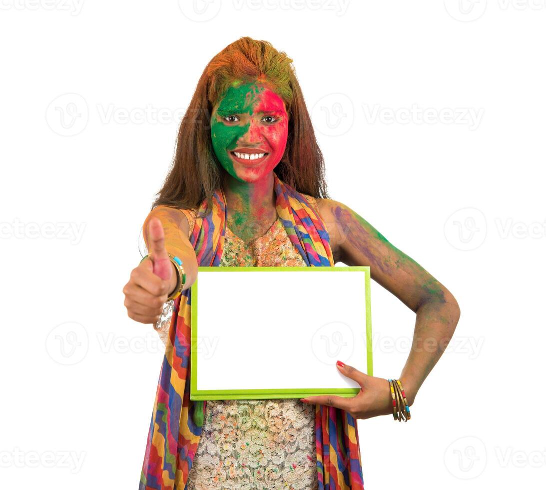 Girl holding a white signboard with face painted with color in Festival of Colour Holi. Isolated portrait photo