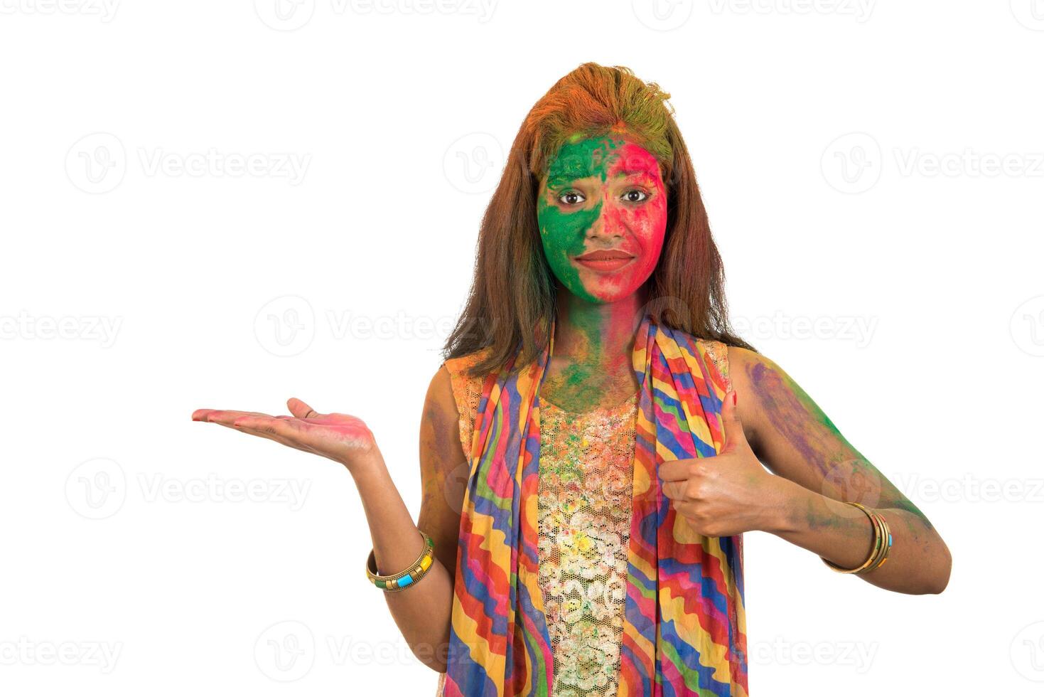 Young girl with a colorful face holding and presenting something on the hand with a happy smiling on occasion of Holi festival. Festival and technology concept. photo