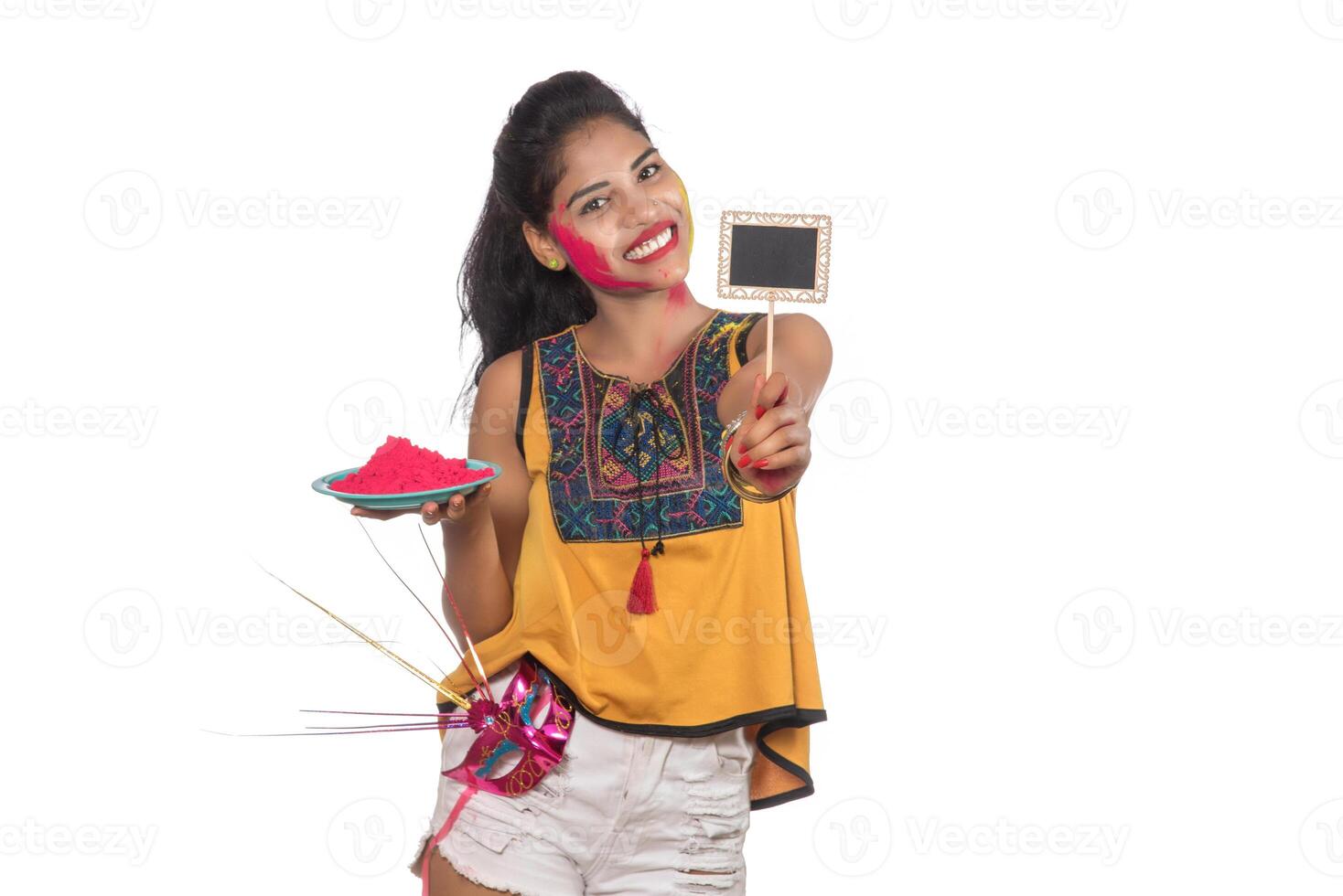 Beautiful young girl holding powdered color in a plate with a carnival mask and small signboard on the occasion of the Holi festival. photo