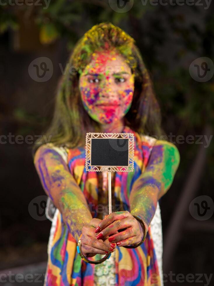 Young girl holding the small board on the occasion of Holi festival with faces painted with powdered colors, with a colour splash. photo