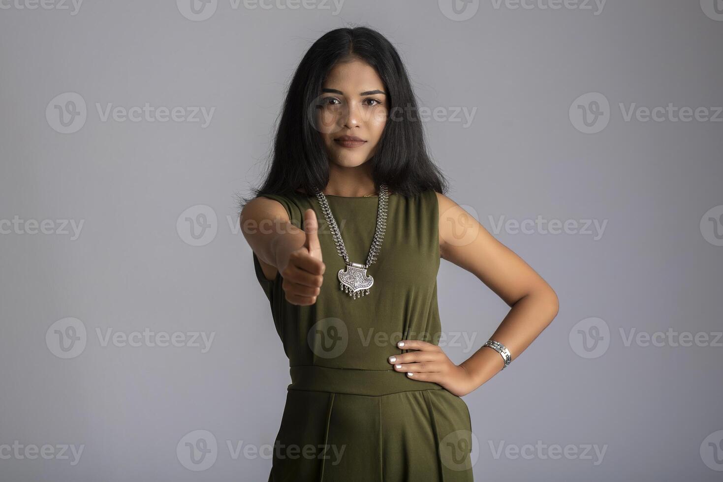 Young smiling girl showing ok sign or thumbs up on a grey background photo