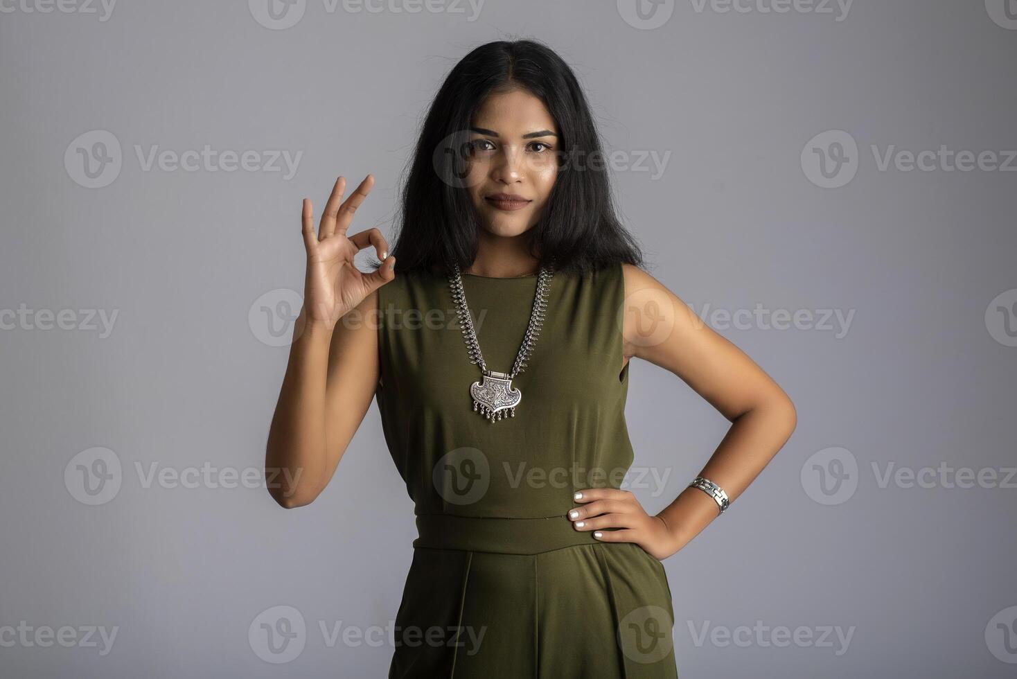 Young smiling girl showing ok sign or thumbs up on a grey background photo