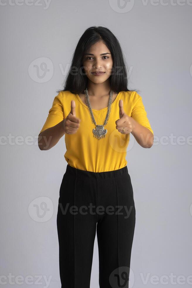 Young smiling girl showing ok sign or thumbs up on a grey background photo